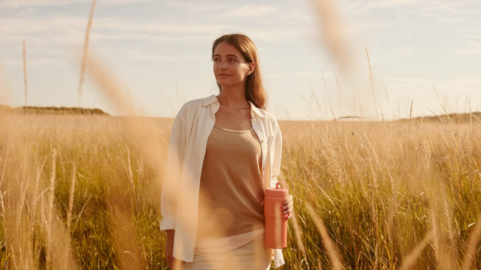 A woman standing in a golden meadow at sunset, looking ahead calmly