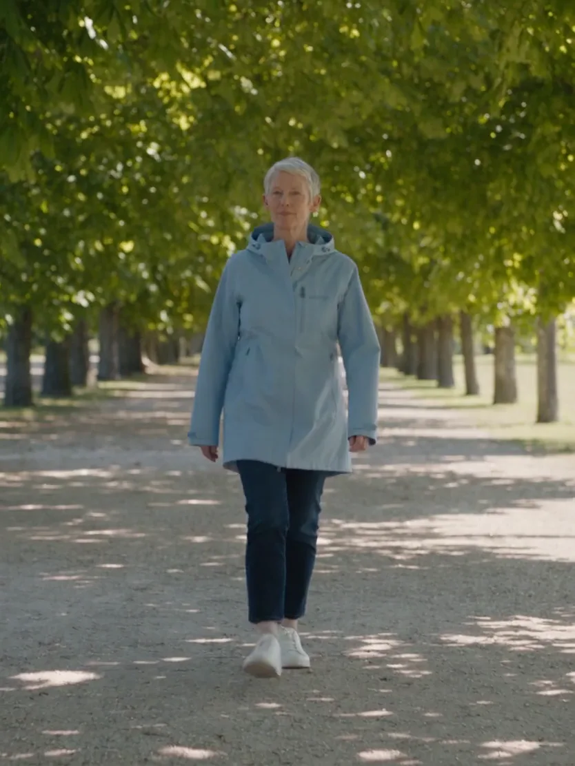 A woman in a light blue jacket walking along a tree-lined park path
