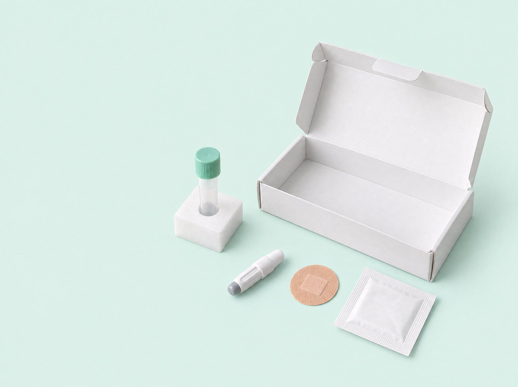 An open white test kit box laid out with a capped sample tube in its holder, a lancet, a plaster and a wipe