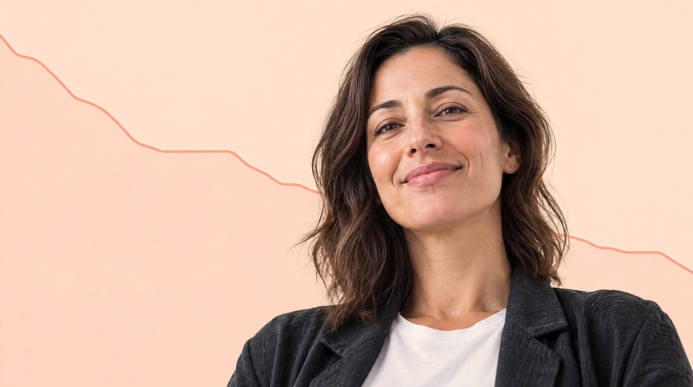 A woman in a white t-shirt and dark jacket smiling, on a plain peach backdrop with a falling chart line behind her